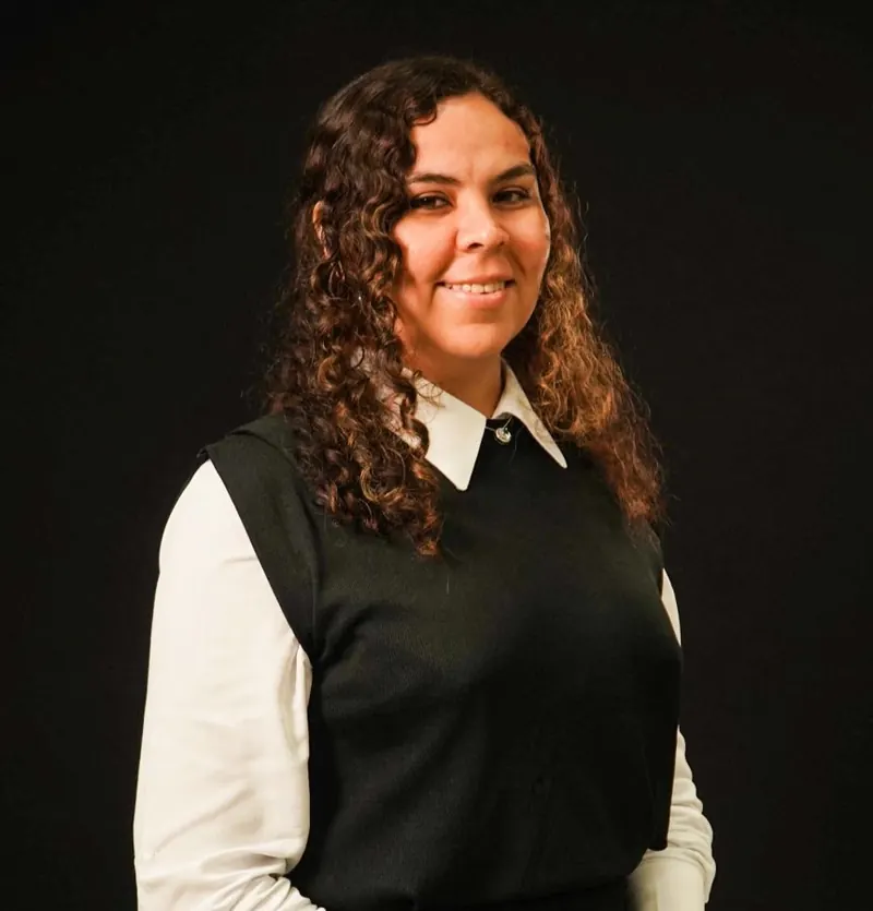 Ana Menires sorrindo, de camisa branca e colete preto